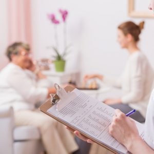 Nurse making notes to medical results with elder woman at the background